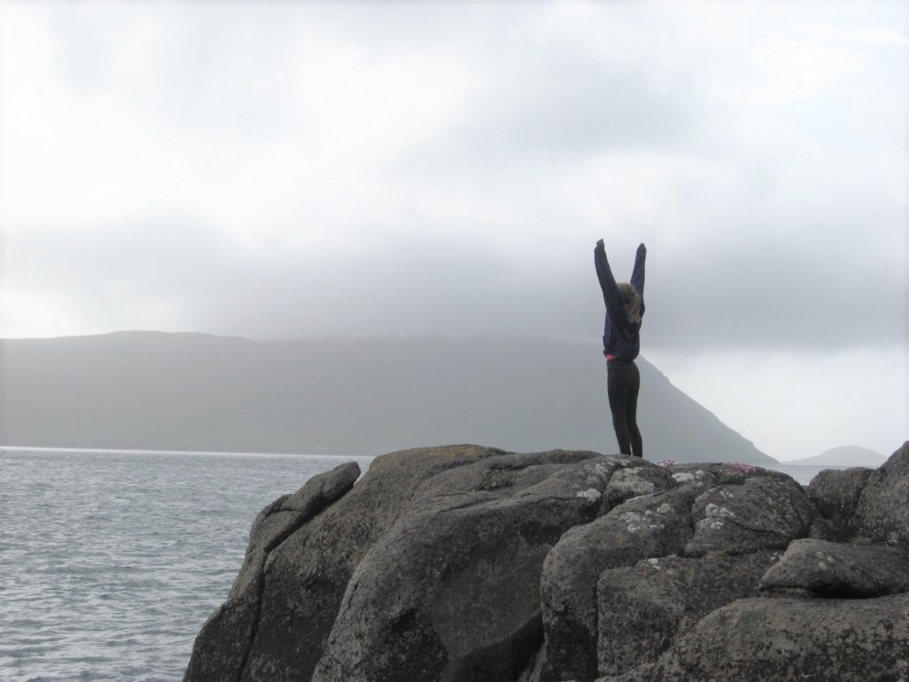 Ung kvinde med armene oppe på en færøsk klippe ud til havet