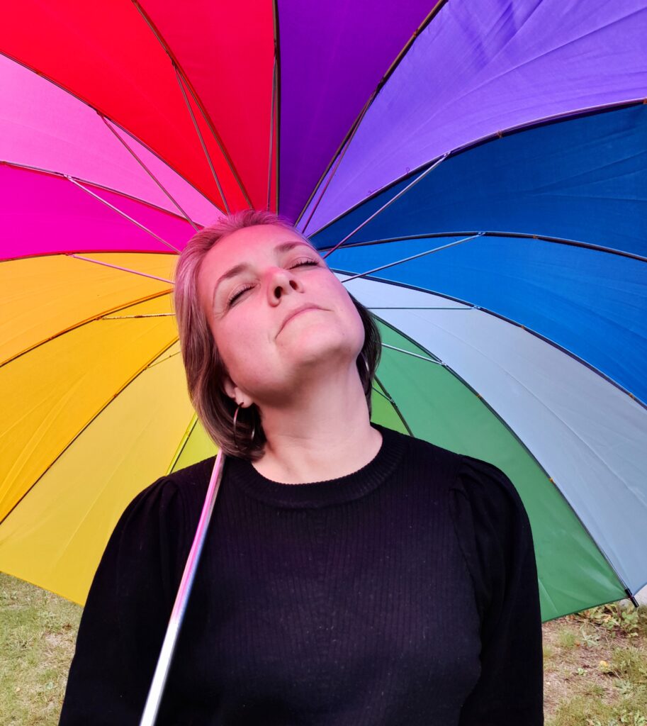 Eva med lukkede øjne foran regnbueparaply