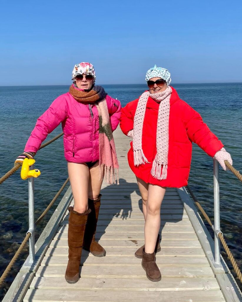To damer i farverigt vintertøj på en badebro