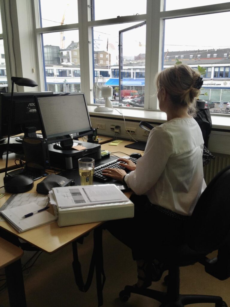 Pernille Højgaard siddende ved et skrivebord foran en compter, tydeligt travlt optaget af sit arbejde
